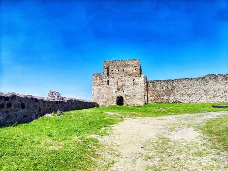 A majestic stone fortress overlooks a vibrant green field while nestled under a bright blue sky, showcasing its historical significance.
