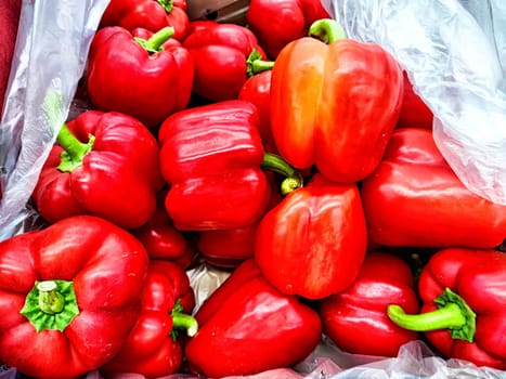 Vibrant red bell peppers are stacked together in a basket at an outdoor market, showcasing their freshness and color.