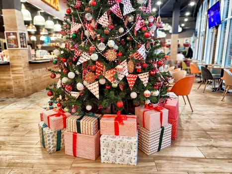 Decorated Christmas tree in a cozy cafe with colorful ornaments and neatly wrapped presents at the base, creating a festive atmosphere.