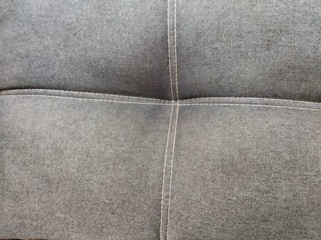 A smooth gray fabric features a textured pattern with visible stitching, ideal for showcasing interior design projects or upholstery work.