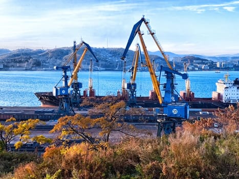 Nahodka, Russia - October 13, 2023: Cranes are actively unloading cargo from large vessels at bustling port as dawn breaks over the calm waters