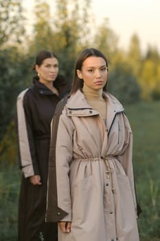 Two stylish girls in raincoats in an apple orchard. Fashion show in an orchard.