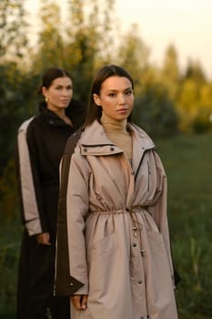 Two stylish girls in raincoats in an apple orchard. Fashion show in an orchard.