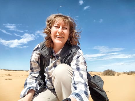 A middle aged woman enjoys the warm sunshine while seated on the sand, surrounded by the vast desert landscape.