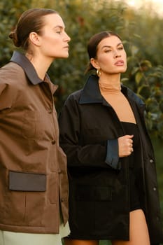 Two stylish girls in jackets at a fashion show in the apple orchard. Fashion show in the garden.