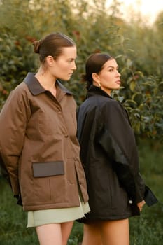 Two stylish girls in jackets at a fashion show in the apple orchard. Fashion show in the garden.