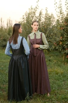 Two stylish girls in dresses with ties in the summer garden. Fashion show in nature.