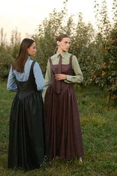 Two stylish girls in dresses with ties in the summer garden. Fashion show in nature.