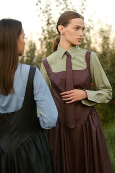 Two stylish girls in dresses with ties in the summer garden. Fashion show in nature.