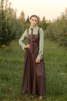 A stylish girl in a dress with a tie in a summer garden. A fashion show in nature.