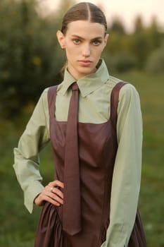 A stylish girl in a dress with a tie in a summer garden. A fashion show in nature.