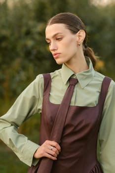 A stylish girl in a dress with a tie in a summer garden. A fashion show in nature.