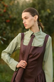 A stylish girl in a dress with a tie in a summer garden. A fashion show in nature.