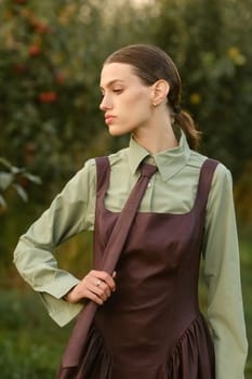 A stylish girl in a dress with a tie in a summer garden. A fashion show in nature.
