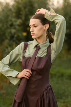 A stylish girl in a dress with a tie in a summer garden. A fashion show in nature.