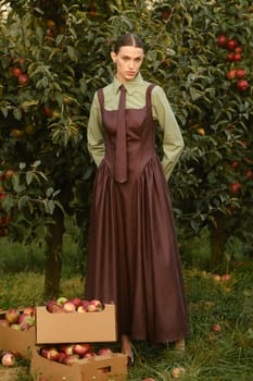Portrait of a beautiful girl, stylishly dressed, with apples in the garden. A girl stands near the collected red apples in the garden.