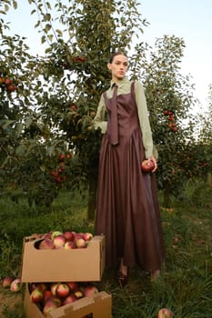 Portrait of a beautiful girl, stylishly dressed, with apples in the garden. A girl stands near the collected red apples in the garden.