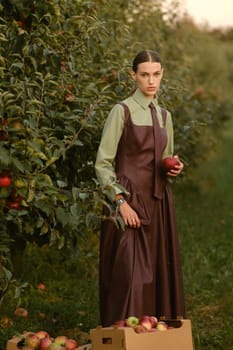 Portrait of a beautiful girl, stylishly dressed, with apples in the garden. A girl stands near the collected red apples in the garden.