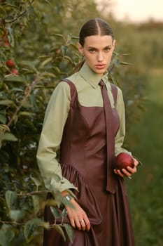 Portrait of a beautiful girl, stylishly dressed, with apples in the garden. A girl stands near the collected red apples in the garden.