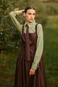 A stylish girl in a dress with a tie in a summer garden. A fashion show in nature.