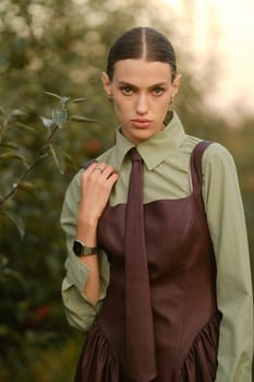 A stylish girl in a dress with a tie in a summer garden. A fashion show in nature.