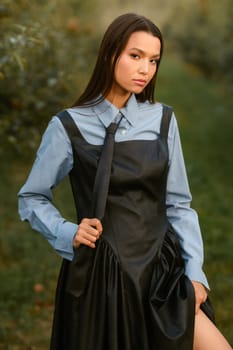 A stylish girl in a dress with a tie in a summer garden. A fashion show in nature.