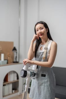 A beautiful young woman happily cleaning her modern home with a vacuum cleaner, showcasing a bright and stylish living room.