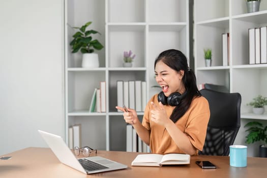 A young female employee celebrates success at her desk, expressing joy and excitement in a modern office setting.