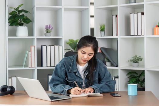 A young woman diligently doing homework at her desk with a laptop and books, creating a productive study environment.