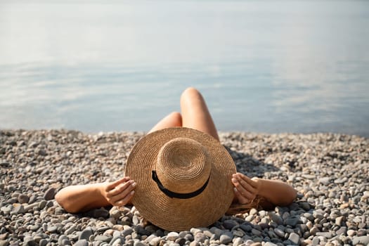 A woman is laying on the beach wearing a straw hat. She is relaxed and enjoying the sun