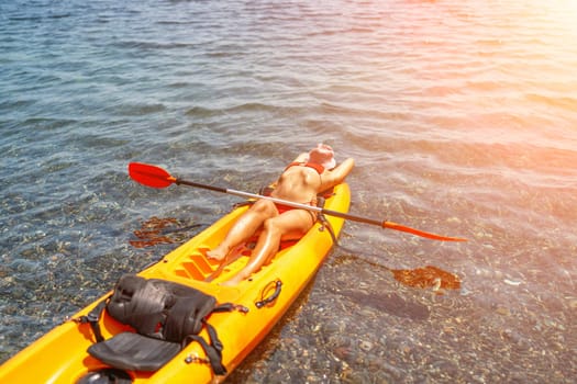 A woman is laying on a kayak in the water. The kayak is orange and has a paddle on it. The woman is wearing a red hat