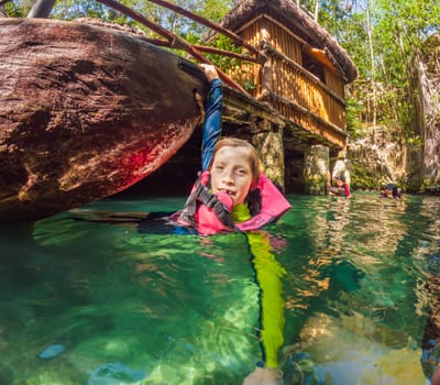 09.12.24, Playa Del Carmen, Mexico: Boy tourist in the water of a cenote at Xcaret park wearing a marked life jacket. Mexican tourism in natural parks. Adventure, childhood exploration, and eco-tourism concept in Quintana Roo.