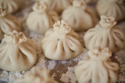 A selection of freshly made Georgian khinkali arranged on a floured table, ready for cooking. Captured in close-up detail, this image showcases the artistry of handmade dough folding.