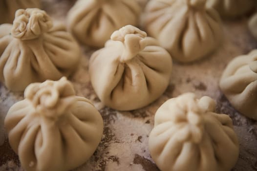 Freshly prepared Georgian Khinkali dumplings are shown on a floured surface, ready to cook.