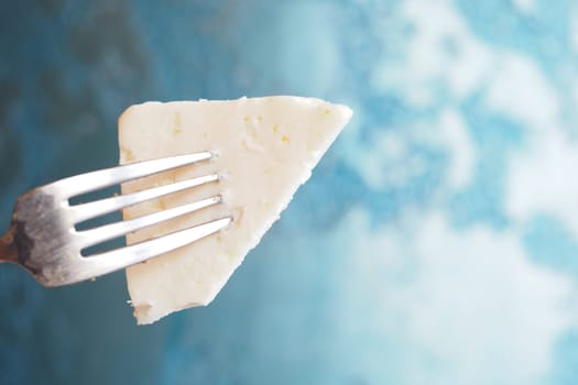 A tantalizing piece of cheese lifted by a fork, set against a vibrant blue backdrop.