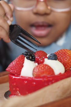 A small child is eagerly reaching out towards a berrytopped dessert with a shiny fork in hand