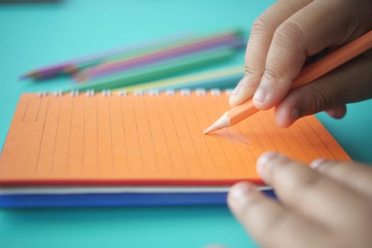 A young child is happily drawing with colorful pencils on a vibrant and attractive notepad