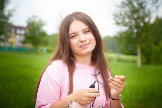 Portrait of young pretty woman with long brown hair and he listens to music with headphones. A blogger on a walk hosts a podcast