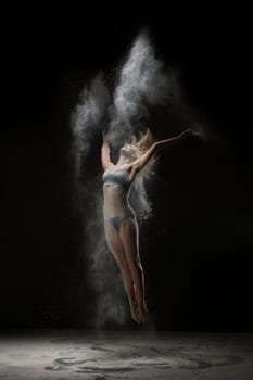 Young girl in lingerie gracefully jumping in white dust cloud shot in a dark room