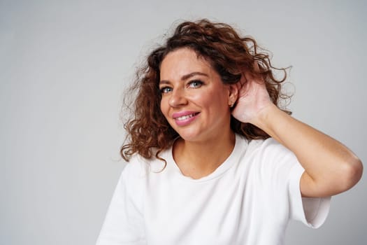 A woman with curly hair smiles while touching her ear, indoors close up
