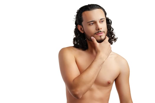 Young man with curly hair thoughtfully posing against a plain background in a studio setting