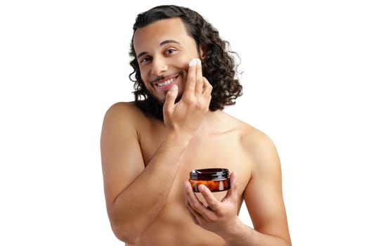 A young man applying skincare cream on his face with a focused expression, demonstrating personal grooming at home close up
