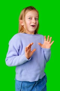 A young girl expresses surprise while smiling, with bright green background and cozy sweater