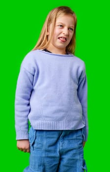A young girl with a playful expression stands against a vivid green background in studio