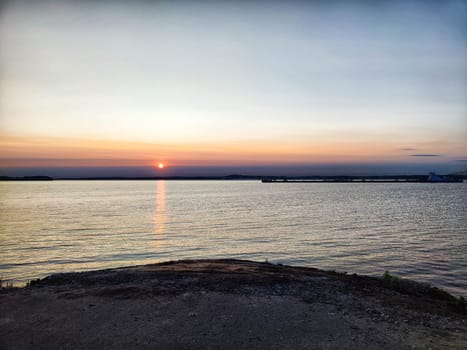 A tranquil evening as the sun sets over the water, casting a warm glow across the horizon.