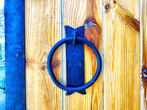 A metal ring knocker is mounted on a rustic wooden door, showcasing craftsmanship and detail in a historic setting.
