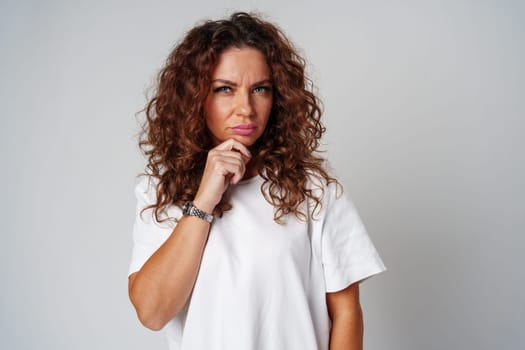 Woman with curly hair thoughtfully pondering in a neutral setting close up
