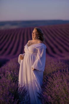 Woman poses in lavender field at sunset. Happy woman in white dress holds lavender bouquet. Aromatherapy concept, lavender oil, photo session in lavender.