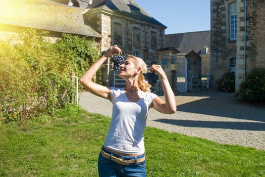Young blonde girl holding grape in front of old French buildings in Provence, France