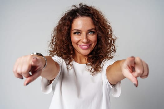 A young woman with curly hair playfully points towards the camera in a bright studio setting